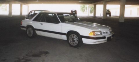 1992 Ford Mustang - A white 1992 Ford Mustang is seen from a three-quarter front view in a parking garage, with another vehicle visible in the background.