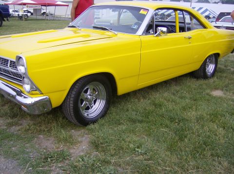 1970 Ford Ranchero - A bright yellow coupe with aftermarket wheels sits on a grassy field, possibly at a car show.