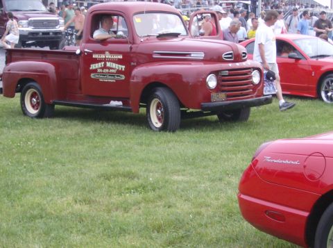 1970 Ford Ranchero - A vintage red pickup truck is parked on a grassy field with other vehicles in the background.