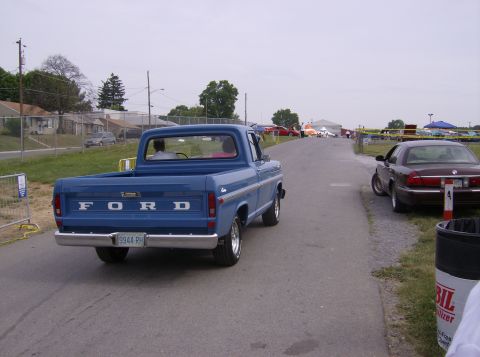 1970 Ford Ranchero - Rear view of a blue Ford pickup truck, likely from the early 1970s, with another car visible on the side of the road.