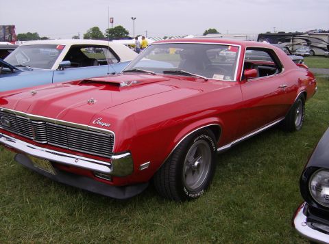 1970 Ford Ranchero - A red 1969 Mercury Cougar is parked on a grassy field, with other vehicles visible in the background.