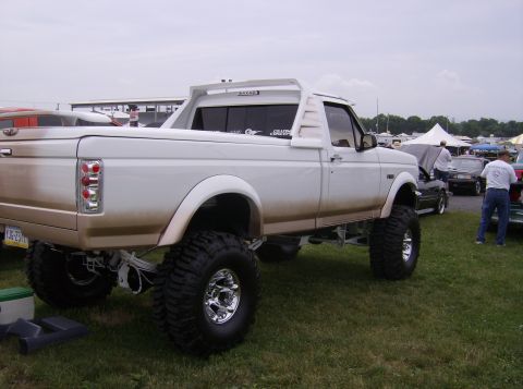 1970 Ford Ranchero - A lifted white pickup truck with a custom rear spoiler and large tires is parked on grass at an outdoor event.