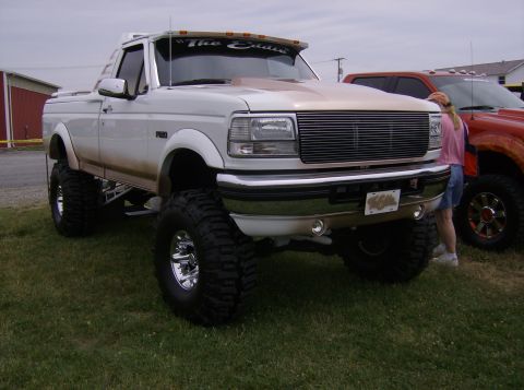 1970 Ford Ranchero - Lifted white pickup truck with custom grille and large tires. Another truck is visible to the right.