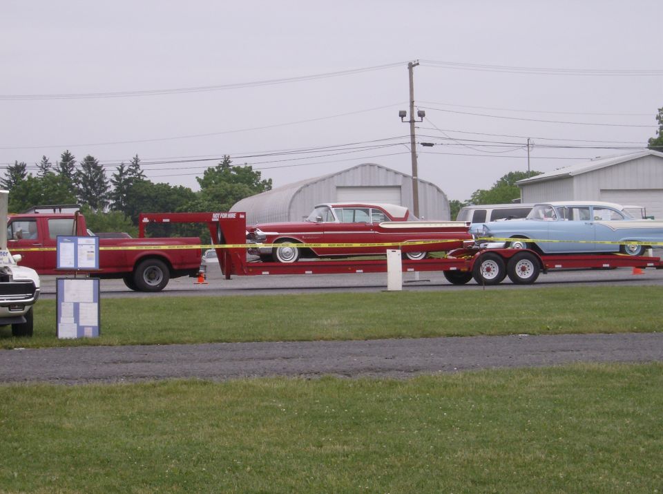 Red pickup truck towing a trailer carrying a red classic car and a blue classic car