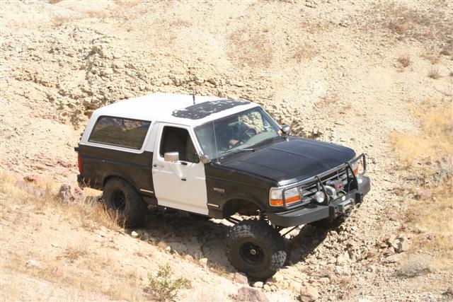 Two-tone black and white Ford Bronco with off-road tires navigating a rocky incline