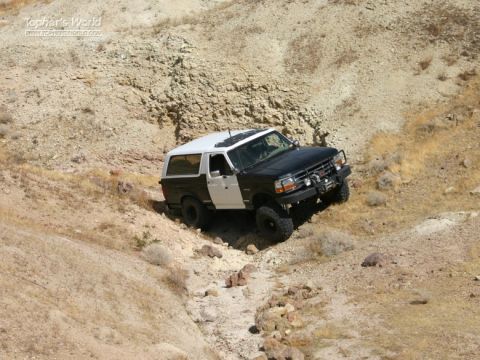 1994 Ford Bronco - 1994 Ford Bronco navigates a challenging off-road trail on a dry, rocky incline.