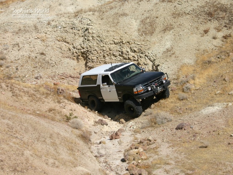 1994 Ford Bronco driving down a dry, rocky creek bed on a dirt hill