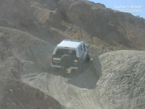 1994 Ford Bronco - White SUV navigates a dusty, rocky incline on a sunny day.