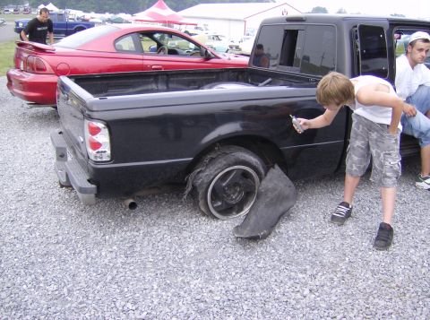 1970 Ford Ranchero - This black pickup truck has a severely damaged rear tire and a loose fender liner. Another car is parked nearby.