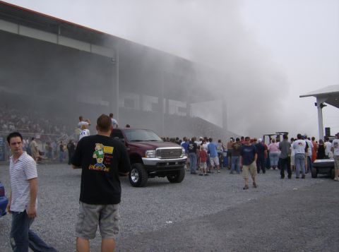 1970 Ford Ranchero - A maroon pickup truck is engulfed in smoke during an event, with a crowd gathered around.