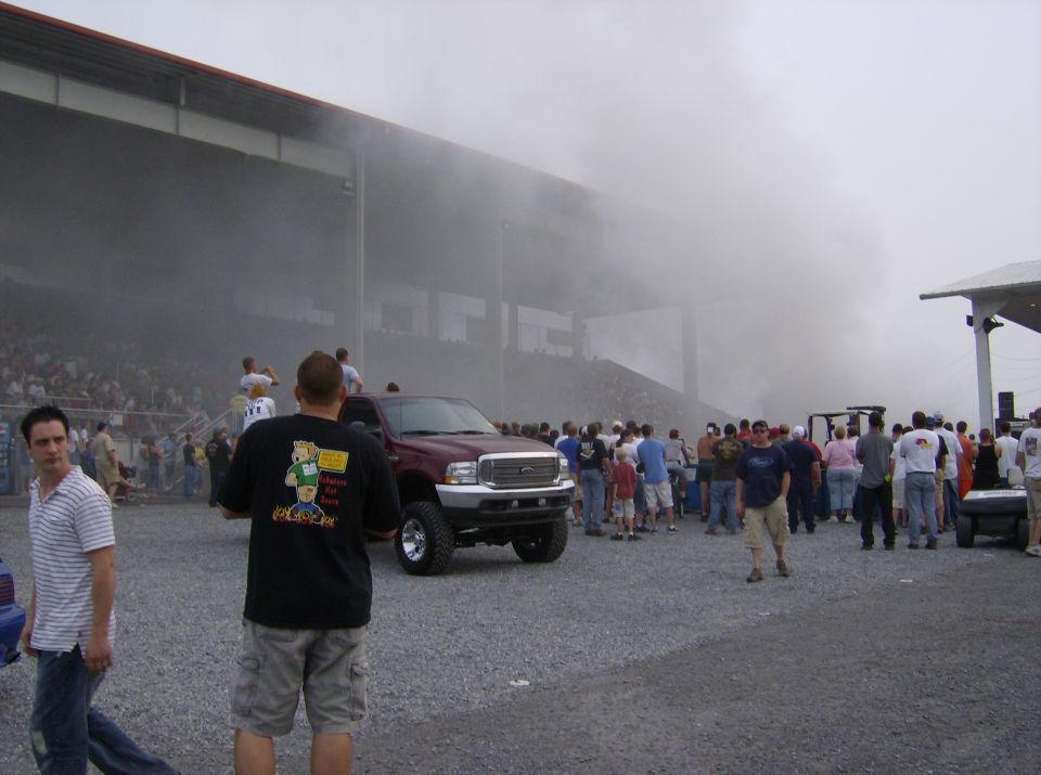 Maroon pickup truck with large grille, surrounded by smoke and spectators