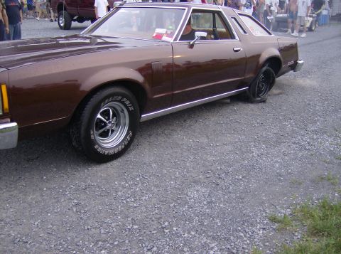 1970 Ford Ranchero - Brown coupe with a flat rear tire parked on a gravel lot. Appears to be a 1977 Ford Thunderbird.