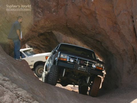 1994 Ford Bronco - Two modified Ford trucks navigate a tight passage in a rocky canyon.