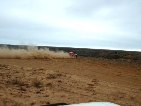 1996 Ford Bronco - A red off-road vehicle races across a dusty desert landscape, leaving a trail of dust in its wake.