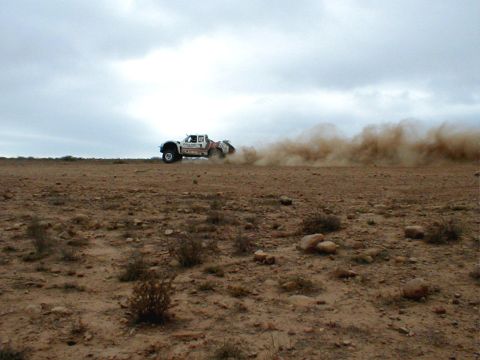 1996 Ford Bronco - Desert racing truck speeds across a dry, barren landscape, creating a massive dust plume.