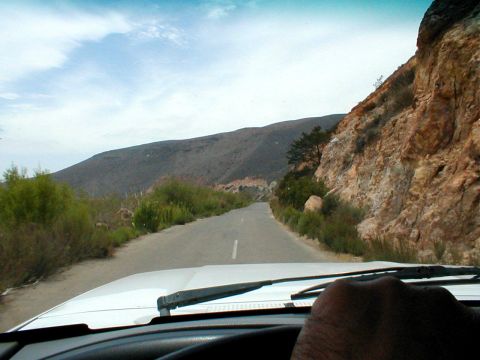 1996 Ford Bronco - View from inside a vehicle driving on a road through a desolate, mountainous terrain under a partly cloudy sky.
