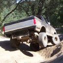 1989 Ford Bronco - This pickup truck is navigating a steep dirt incline, with its front wheels lifted.