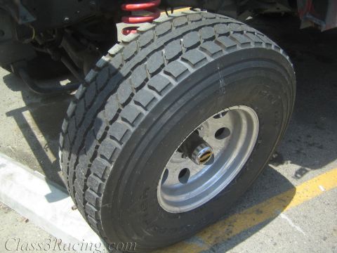 1990 Ford Bronco - Close-up of a large all-terrain truck tire on a silver steel wheel, with a red coilover spring visible in the wheel well above.