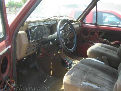 1990 Ford Bronco - gutted interior of a project truck shows an exposed dashboard, steering column, gauge cluster and cloth bucket seats with wiring hanging lo…