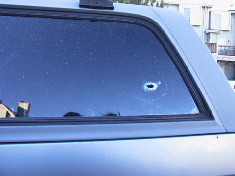 1994 Ford Bronco - The rear quarter window of a light blue SUV has a bullet hole and visible scratches.