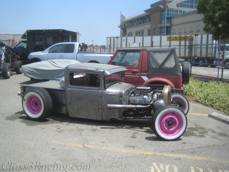 Bare-metal rat-rod pickup with exposed engine and pink whitewalls in lot