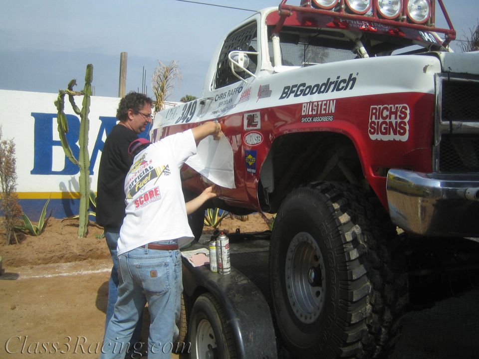 Man applying decals to a red and white BFGoodrich-sponsored off-road race truck