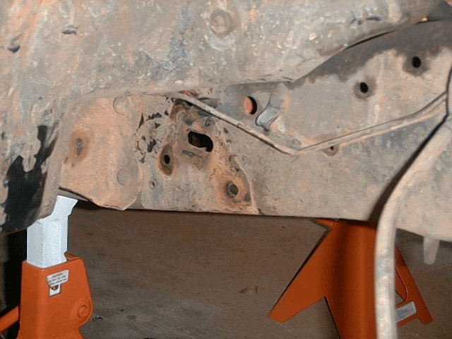 Rusty frame and body mount underside of a vehicle supported on orange jack stands
