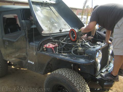 1990 Ford Bronco - person leans into the engine bay of a black Jeep with its hood up, exposed wiring and a red air filter visible.