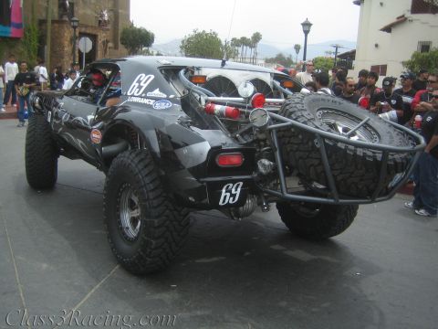 1990 Ford Bronco - black tube-chassis off-road race buggy numbered 69 sits on a street with a rear tire carrier and chase lights, surrounded by onlookers.