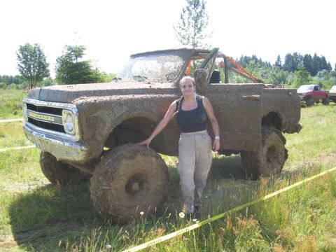 1989 Ford Bronco - A woman poses next to a heavily mud-caked Chevrolet pickup truck during an outdoor event.