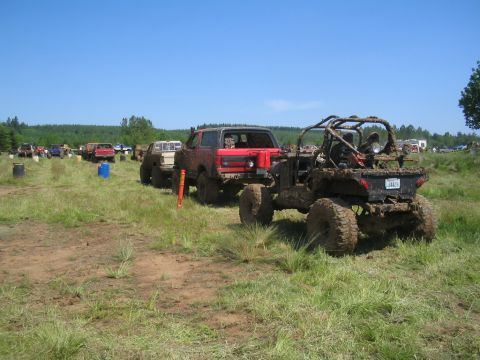 1989 Ford Bronco - Several off-road vehicles are gathered in a grassy field under a clear blue sky, ready for a mud bogging event.