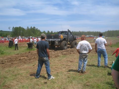 1989 Ford Bronco - A lifted pickup truck navigates a muddy track during an event, with spectators gathered to watch.