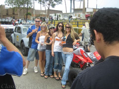 1990 Ford Bronco - group of young women and a man pose around a red racing ATV on a street busy with spectators and off-road vehicles.
