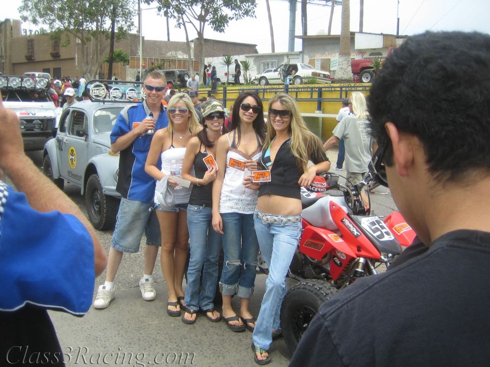 Young women and a man posing by a red racing ATV in a street with race vehicles