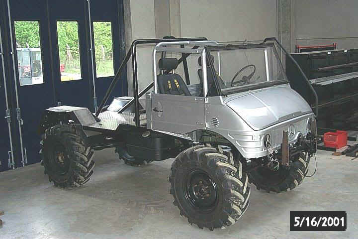 Silver Mercedes-Benz Unimog with large tires and roll cage, viewed from the front-right