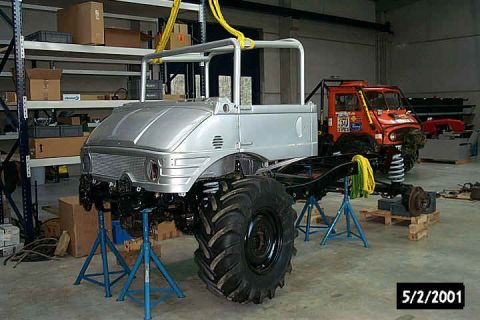 1991 Ford Bronco - A silver truck chassis is elevated on stands, with an orange truck visible in the background. The date 5/2/2001 is stamped on the image.
