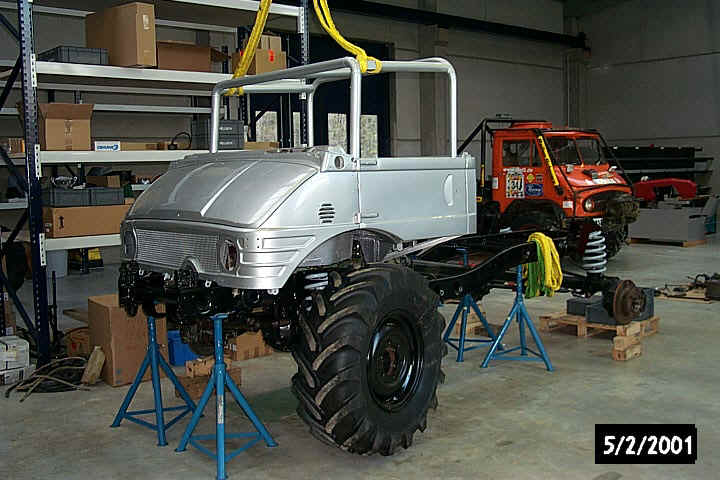 Silver truck chassis on blue stands, orange truck in background. Date 5/2/2001 visible