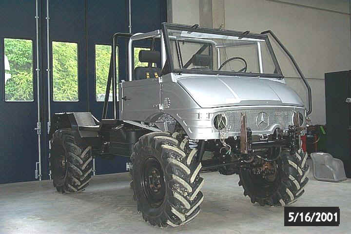 Silver Mercedes-Benz Unimog chassis with large tractor tires, roll cage, and exposed frame