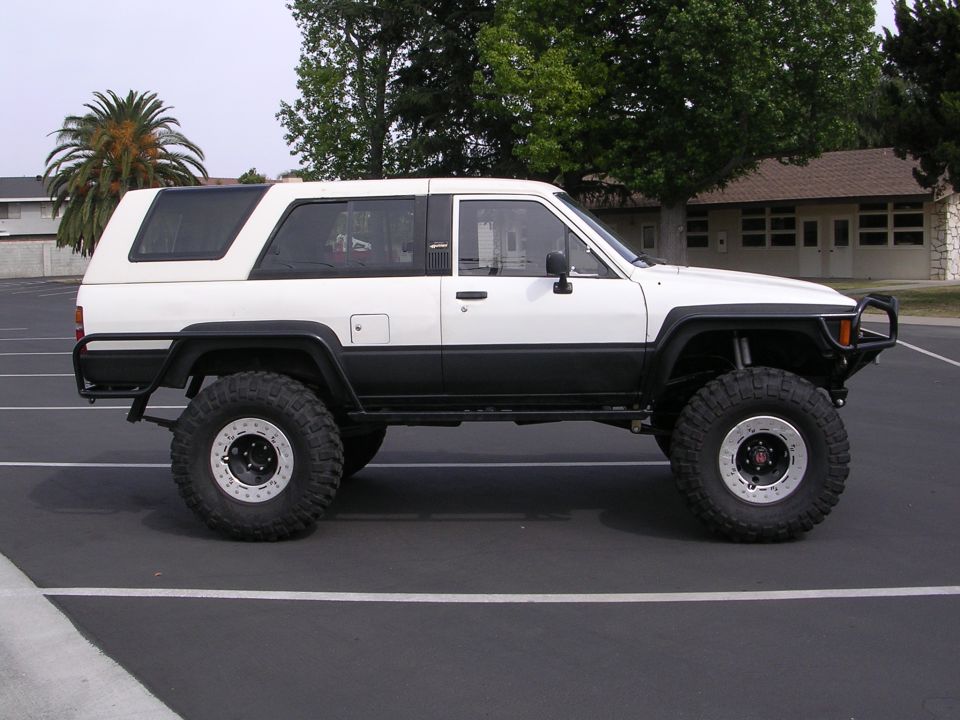 White and black Toyota 4Runner with large off-road tires and custom bumper, viewed from the side