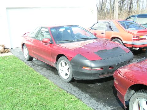 1996 Ford Probe - A red 1996 Ford Probe is parked in front of a garage, partially covered by a car bra.