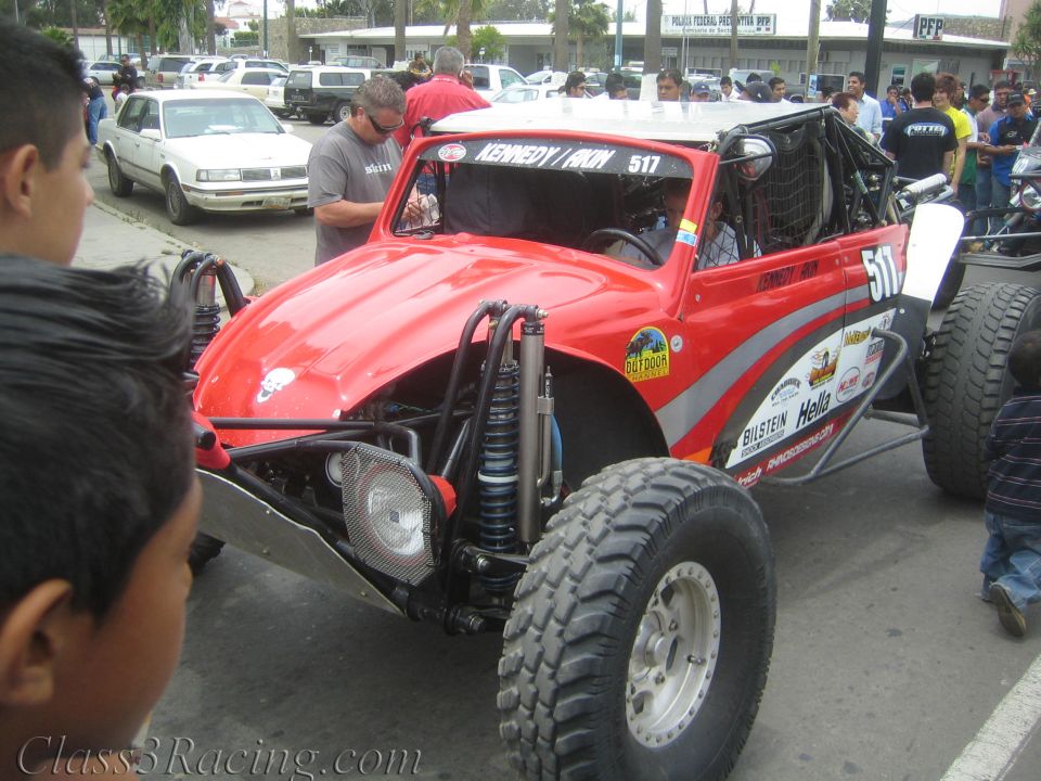 Red tube-frame off-road race buggy numbered 517 parked in a lot with spectators