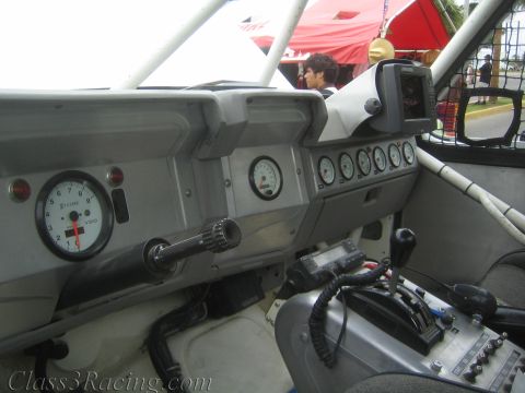 1990 Ford Bronco - stripped interior of an off-road race car showing analog gauges, a mounted GPS unit, a roll cage, and a manual shifter.