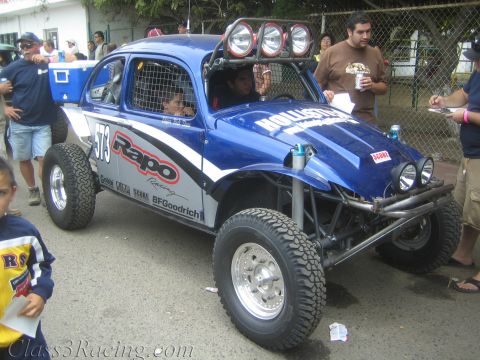 1990 Ford Bronco - blue Baja-prepped Volkswagen Beetle race buggy numbered 573 with a roof light bar and Rapo Racing decals on a street.
