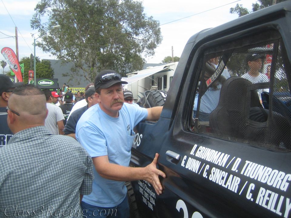 Man gesturing beside a black race vehicle door listing driver names