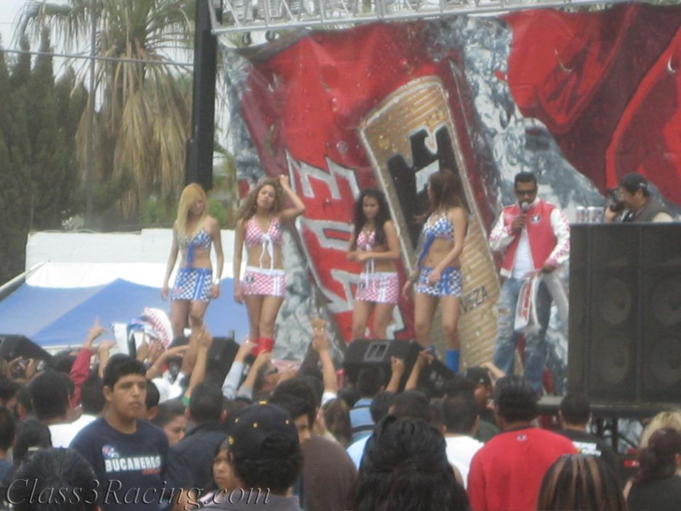 Costumed dancers performing on a stage with a giant beer can backdrop before a crowd