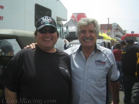 1990 Ford Bronco - Two smiling men pose arm-in-arm at an outdoor event, one in a black cap and tee, the other in a gray work shirt.