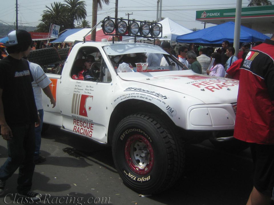 White off-road race truck with roof light bar and Rescue Racing graphics in a crowd