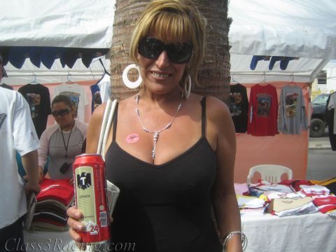 1990 Ford Bronco - blonde woman in sunglasses and a black top holds a red beer can in front of vendor tents selling T-shirts at an outdoor event.