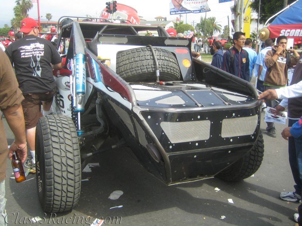 Rear view of a black tube-frame off-road race buggy among a crowd
