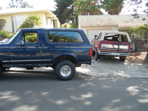1994 Ford Bronco - A dark blue 1994 Ford Bronco is parked in front of a house, with a red convertible SUV also visible in the driveway.